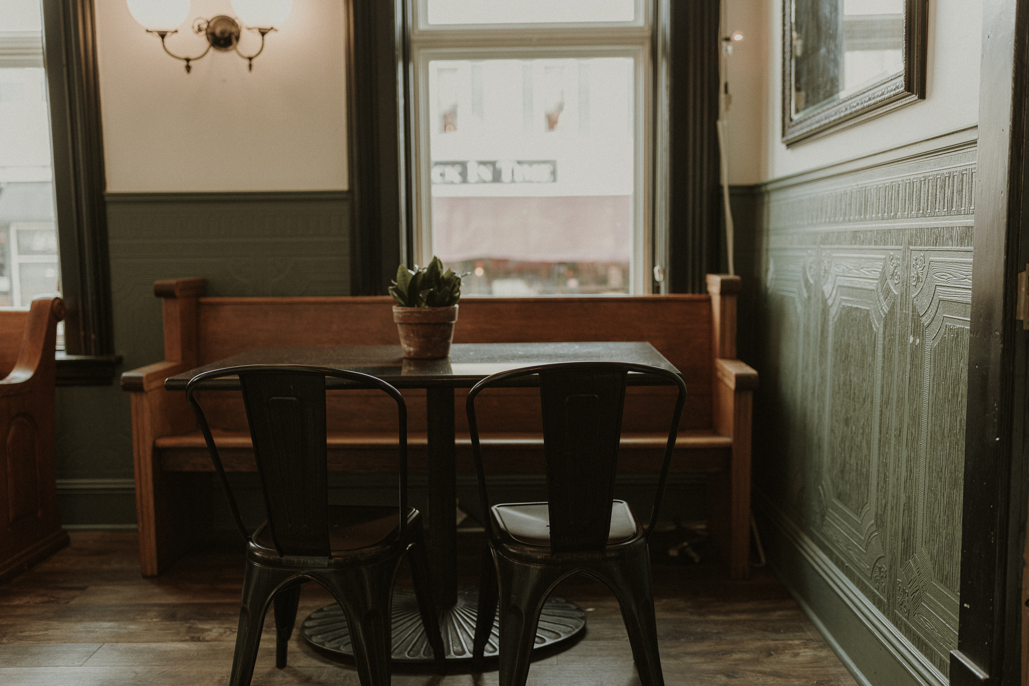 A cozy corner of a coffee shop in Washington, IL, featuring a wooden bench, a small table with a potted plant, and metal chairs, illuminated by natural light streaming through large windows.